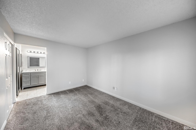 unfurnished room featuring light carpet, a textured ceiling, a sink, and baseboards