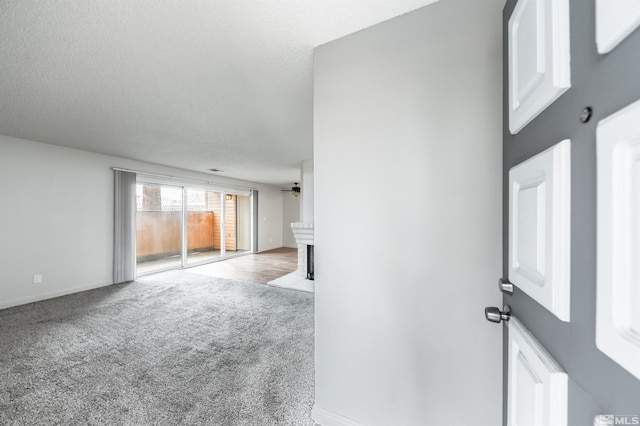 spare room with a textured ceiling, carpet, baseboards, and a brick fireplace