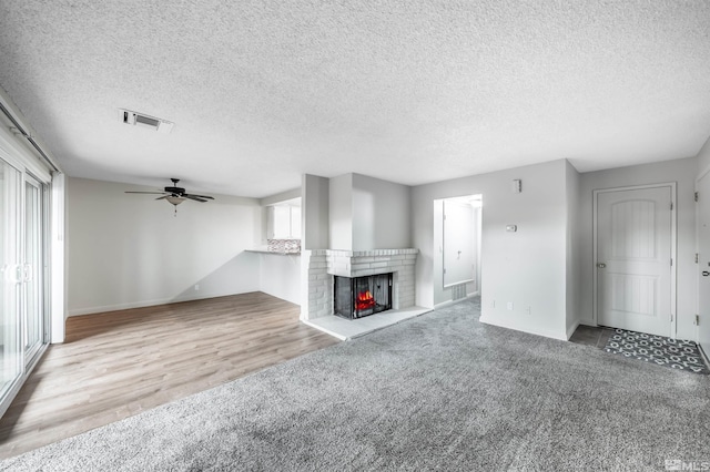 unfurnished living room with carpet, a fireplace, visible vents, a ceiling fan, and a textured ceiling