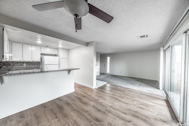 kitchen with a peninsula, visible vents, dark stone counters, and freestanding refrigerator