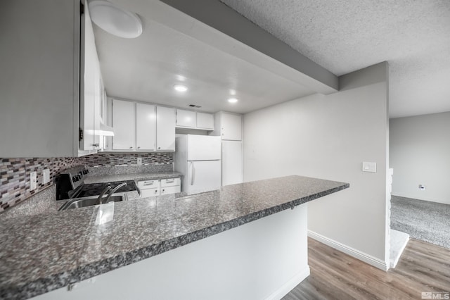 kitchen featuring a peninsula, wood finished floors, stainless steel range with electric cooktop, backsplash, and freestanding refrigerator