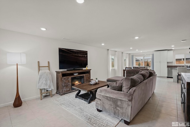 living area featuring light tile patterned floors, baseboards, a glass covered fireplace, and recessed lighting