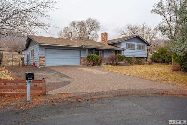 tri-level home with a chimney, an attached garage, fence, decorative driveway, and brick siding