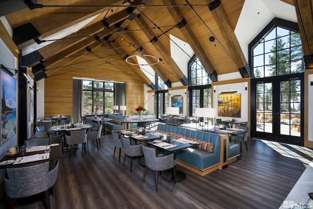 dining room featuring french doors, beam ceiling, wood walls, wood finished floors, and high vaulted ceiling