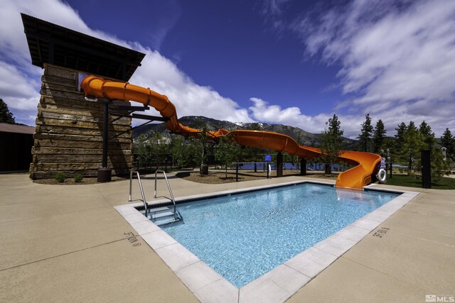 community pool with playground community, a water slide, and a patio area