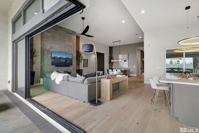 living area with ceiling fan, recessed lighting, a large fireplace, a high ceiling, and light wood-type flooring