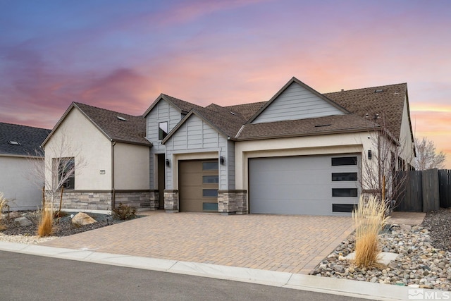 view of front facade with stone siding, a shingled roof, decorative driveway, and an attached garage