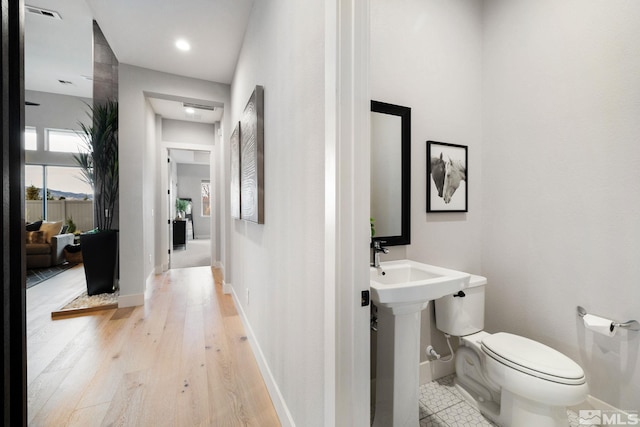 bathroom with toilet, a sink, visible vents, wood finished floors, and baseboards