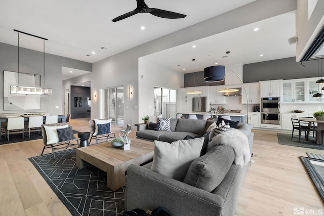 living area featuring light wood-style floors, ceiling fan, and a towering ceiling