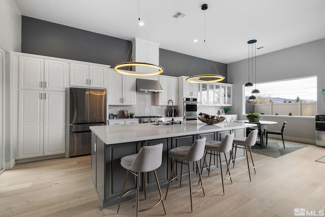 kitchen featuring visible vents, wall chimney exhaust hood, stainless steel appliances, light wood-type flooring, and a sink