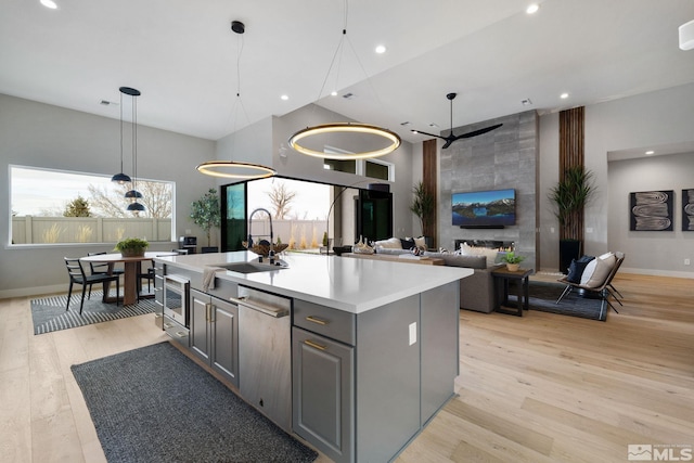 kitchen with a kitchen island with sink, a sink, light countertops, light wood-type flooring, and gray cabinets