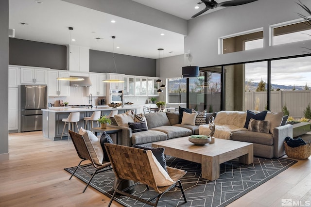 living room featuring ceiling fan, a high ceiling, light wood-style flooring, and recessed lighting