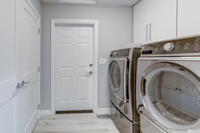 laundry area featuring baseboards, washing machine and clothes dryer, cabinet space, and light wood-style floors