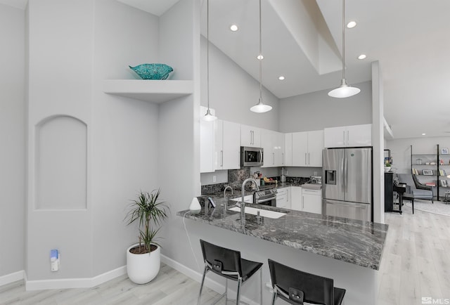 kitchen with dark stone counters, a towering ceiling, appliances with stainless steel finishes, a peninsula, and a sink