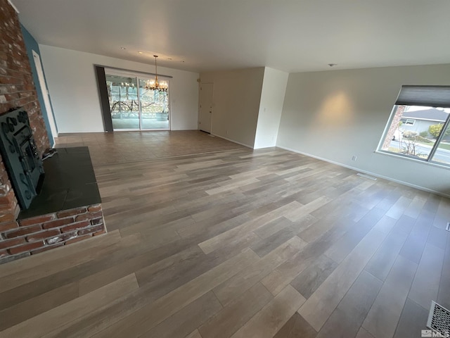 unfurnished living room with a chandelier, a fireplace, plenty of natural light, and wood finished floors