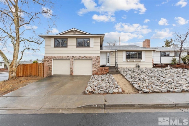 split level home featuring a chimney, fence, concrete driveway, and brick siding