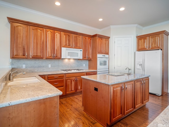 kitchen featuring light stone counters, a center island with sink, a sink, wood finished floors, and white appliances