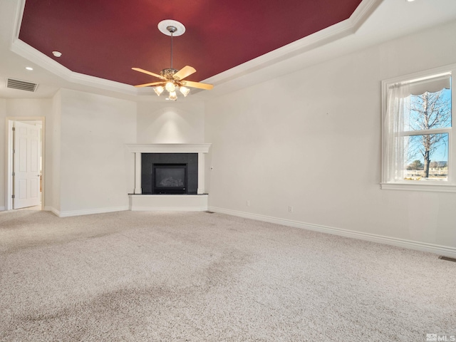 unfurnished living room with carpet floors, a tray ceiling, visible vents, and baseboards