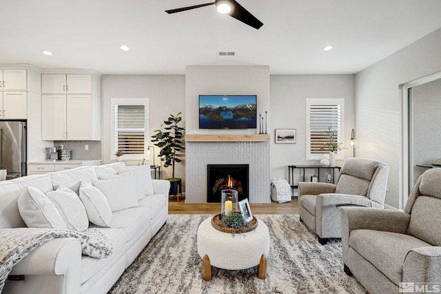 living area with visible vents, a ceiling fan, light wood-style flooring, a brick fireplace, and recessed lighting