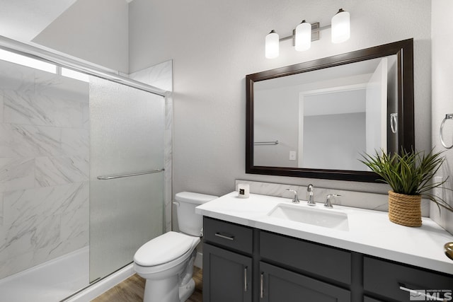 full bath with a stall shower, a textured wall, toilet, wood finished floors, and vanity