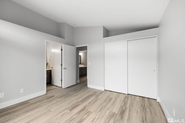 unfurnished bedroom featuring lofted ceiling, light wood-type flooring, baseboards, and a closet