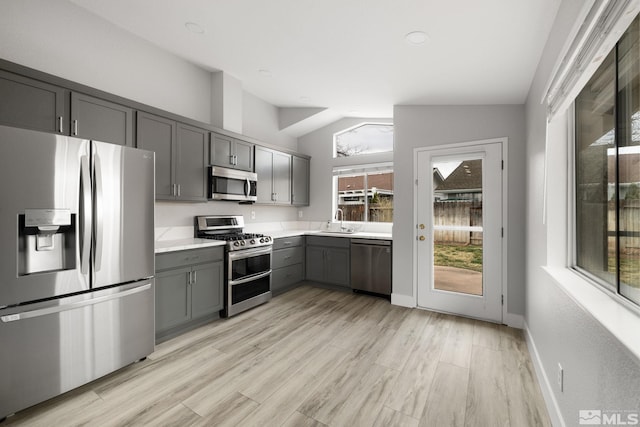 kitchen featuring light countertops, gray cabinetry, appliances with stainless steel finishes, vaulted ceiling, and a sink