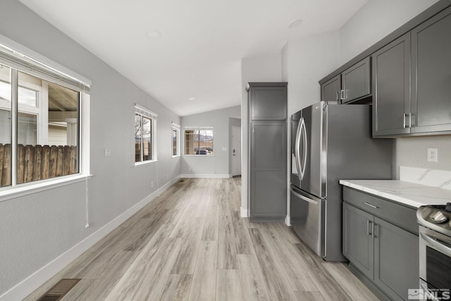 kitchen featuring light stone counters, light wood finished floors, stainless steel appliances, gray cabinetry, and vaulted ceiling