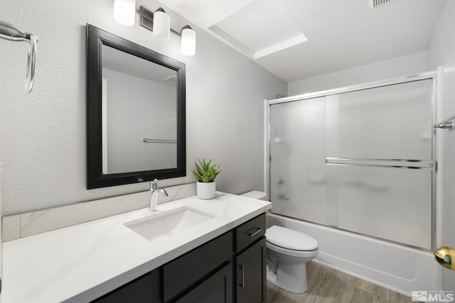 bathroom featuring a textured wall, toilet, wood finished floors, combined bath / shower with glass door, and vanity