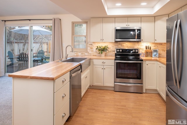 kitchen featuring stainless steel appliances, a sink, a peninsula, and wooden counters