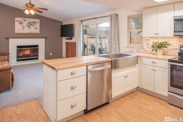 kitchen featuring lofted ceiling, stainless steel appliances, a sink, wood counters, and white cabinets