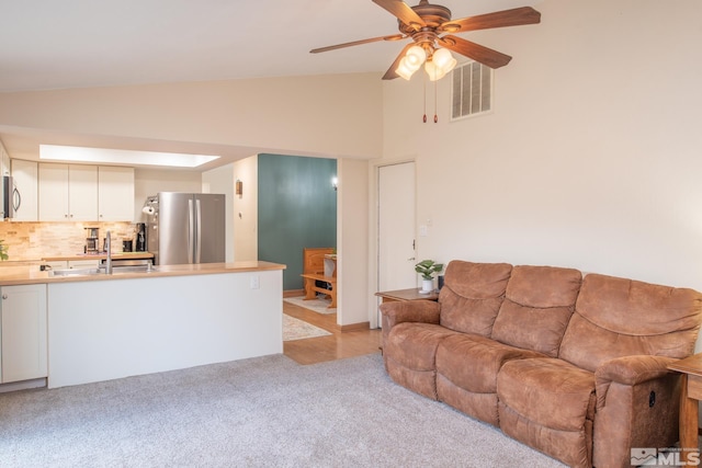 living room featuring ceiling fan, high vaulted ceiling, light colored carpet, visible vents, and a wood stove