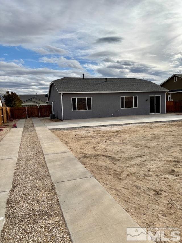 rear view of property with roof with shingles, stucco siding, a patio, and fence