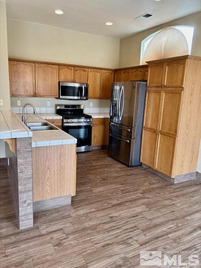 kitchen with tile counters, visible vents, appliances with stainless steel finishes, light wood-style floors, and a sink