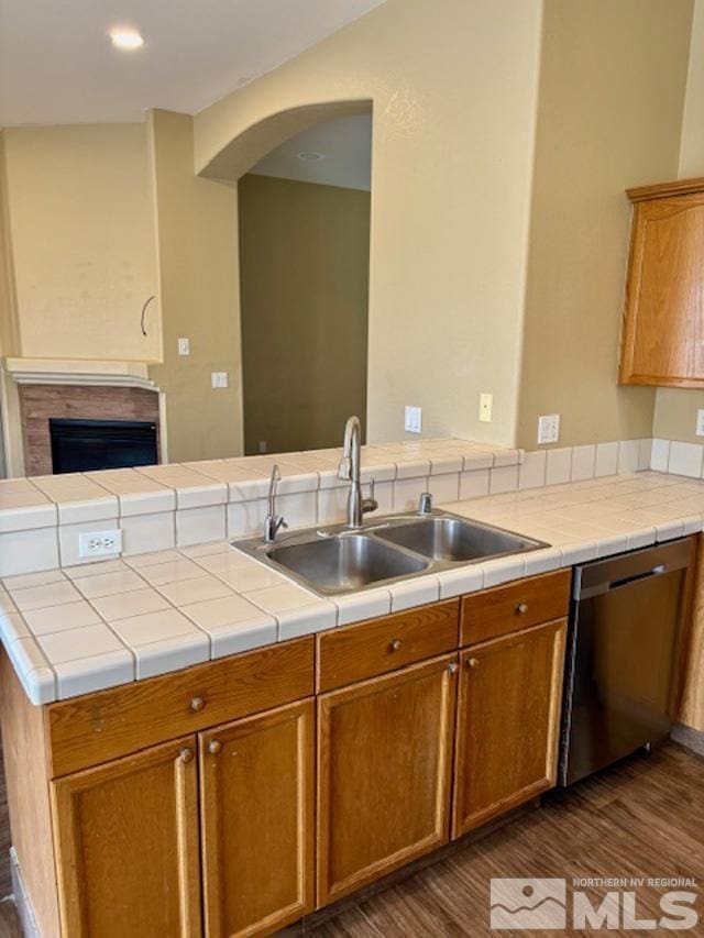 kitchen featuring a tile fireplace, dark wood-type flooring, a sink, light countertops, and stainless steel dishwasher