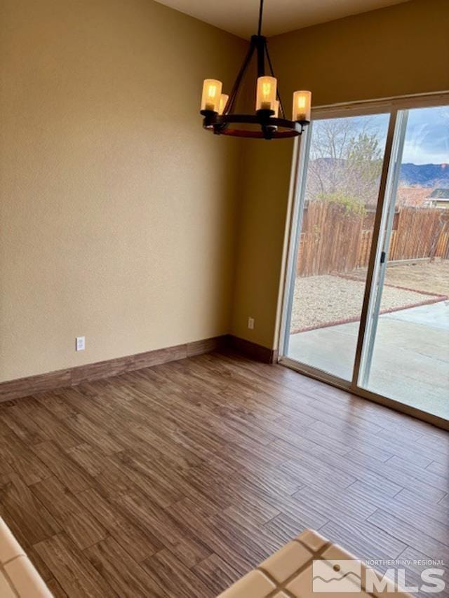 unfurnished room featuring baseboards, wood finished floors, and an inviting chandelier