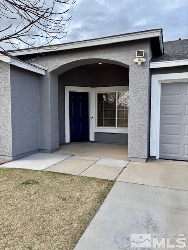 doorway to property with an attached garage and stucco siding