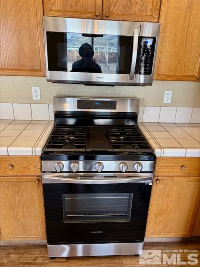 kitchen with tile countertops, light wood-style floors, and appliances with stainless steel finishes