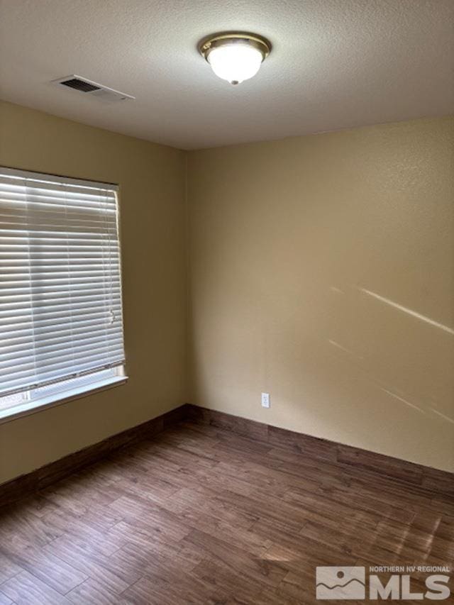 empty room with baseboards, a textured ceiling, visible vents, and wood finished floors