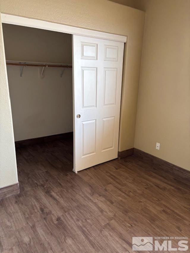 unfurnished bedroom featuring a closet, dark wood finished floors, and baseboards