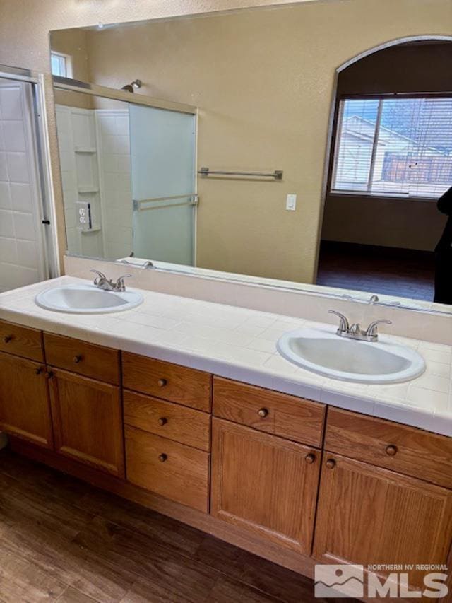 bathroom featuring double vanity, a shower with door, a sink, and wood finished floors