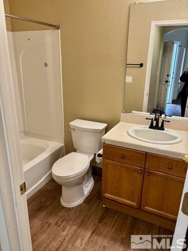 bathroom featuring bathtub / shower combination, a textured wall, toilet, vanity, and wood finished floors