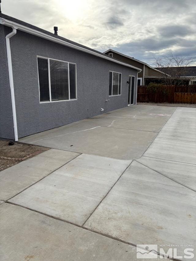 rear view of house with a patio, fence, and stucco siding