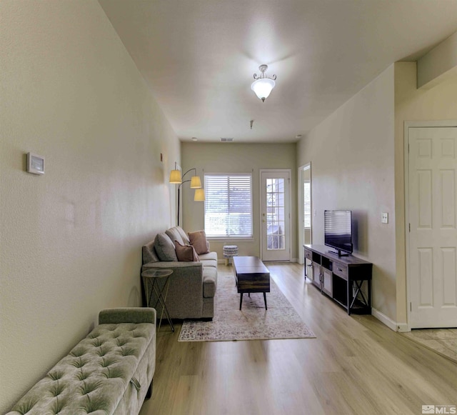 living room with light wood-style floors, visible vents, and baseboards