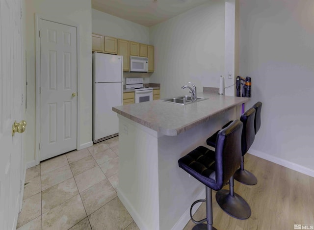 kitchen featuring a breakfast bar area, light tile patterned floors, a sink, white appliances, and a peninsula