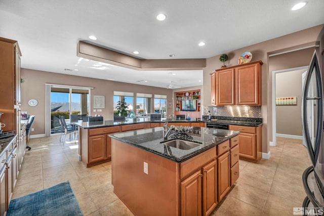 kitchen with tasteful backsplash, an island with sink, dark stone countertops, a peninsula, and a sink