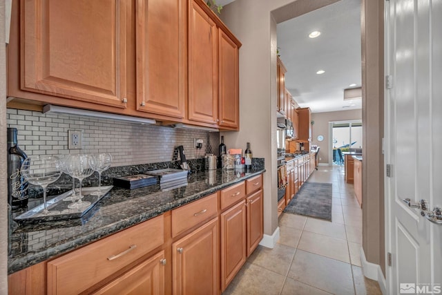 kitchen featuring light tile patterned floors, baseboards, dark stone counters, brown cabinets, and backsplash