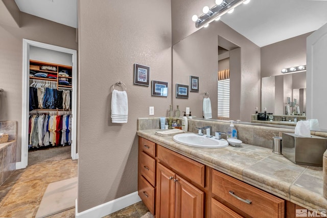 bathroom with a textured wall, baseboards, a walk in closet, and vanity