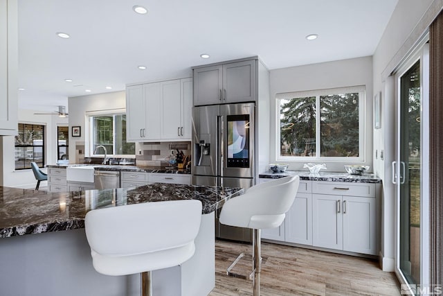 kitchen with recessed lighting, a kitchen breakfast bar, appliances with stainless steel finishes, dark stone counters, and light wood finished floors