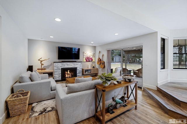 living area featuring a stone fireplace, recessed lighting, wood finished floors, and baseboards