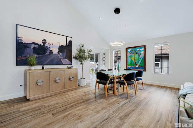 dining room featuring high vaulted ceiling, light wood finished floors, and baseboards